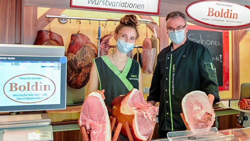 Jens und Lavinia Boldin mit den drei Schinken, von denen sie frisch und vor den Augen der Kunden die Scheiben in gewünschter Stärke herunterschneiden.