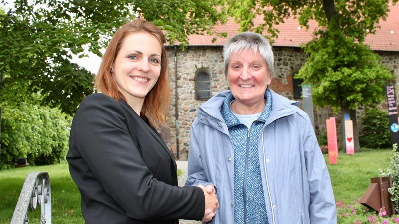 Pastorin Christina Wolf (links) von der Ev.-luth. Kirchengemeinde Hittfeld übergibt Hanne Riemer, Erste  Vorsitzende von BAOBAB – Schüler für Afrika e.V., vor der Hittfelder Mauritiuskirche. | Foto: ein/C. Wöhling