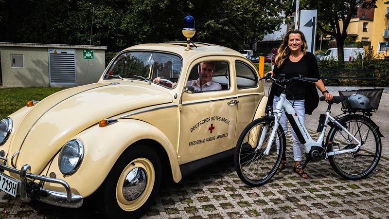 Beide schick: Der 55 Jahre alte Oldtimer des DRK mit Aart Paasman, Geschäftsführer DRK-Sozialstation Harburg, am Steuer und Marta Küster vom DRK-Pflegeteam mit einem nagelneuen E-Bike. | Foto: ein/DRK-Kreisverband Hamburg-Harburg e. V.