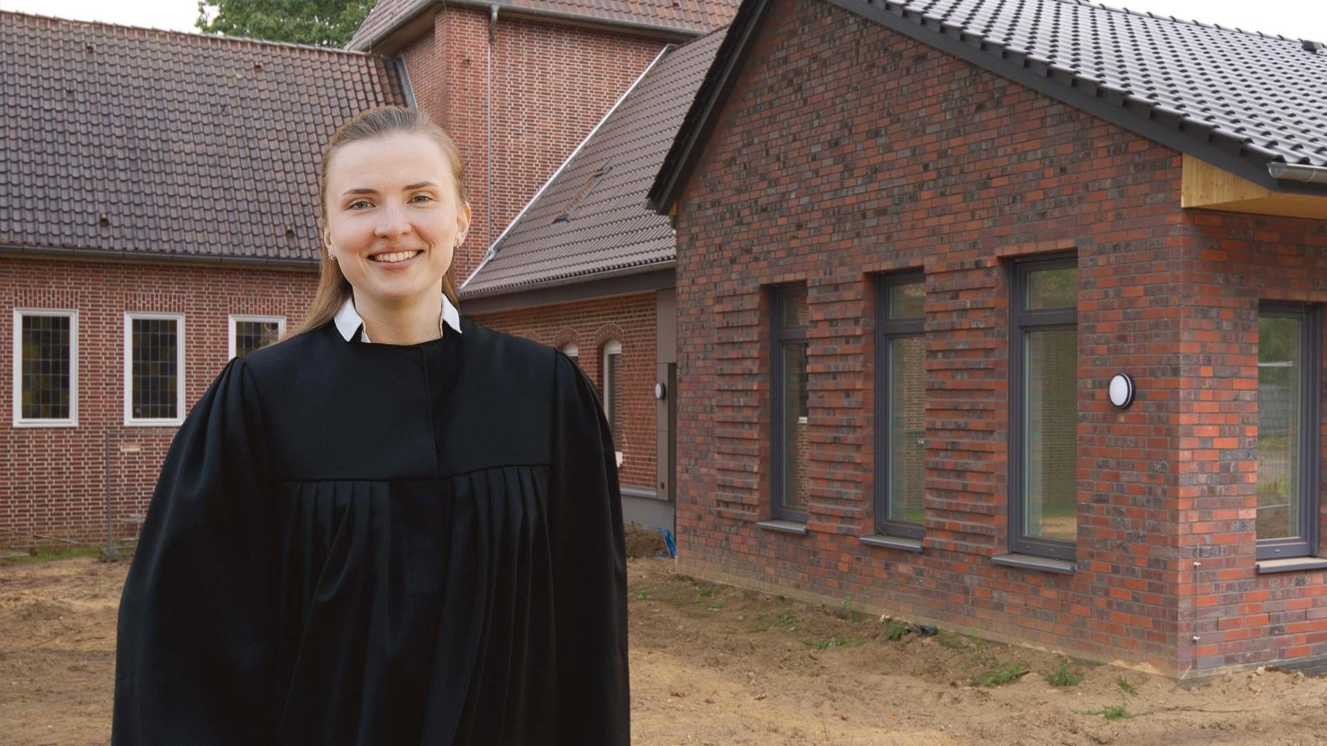 Pastorin Anna-Lena Hübsch vor dem neuen Gemeindehaus und der Kreuzkirche in Sprötze. Foto: H. Gilbert und U. Wagner