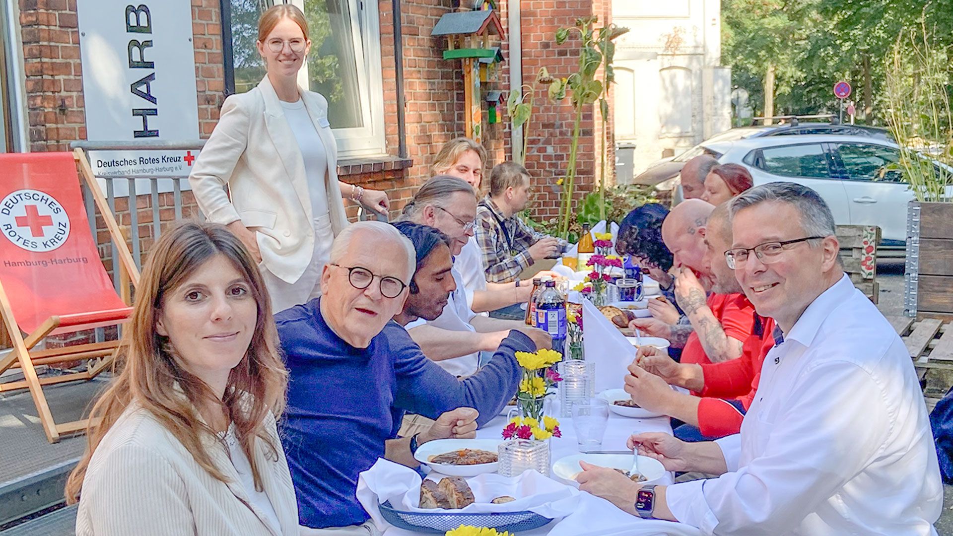 Gäste und Organisatoren vor dem Harburg-Huus des DRK an der weiß-gedeckten Tafel beim Eintopf von Star-Köchin Cornelia Poletto. | Foto. DRK Hamburg-Harburg