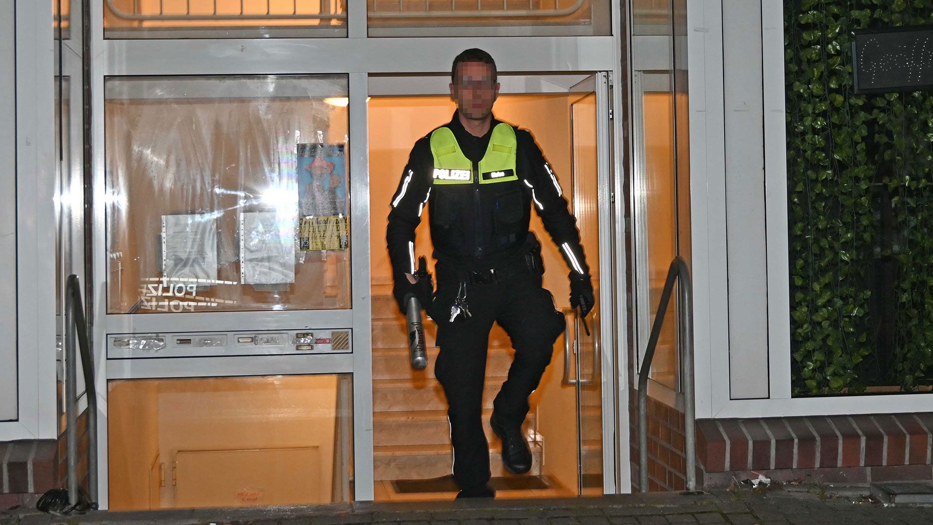 Ein Polizist bringt den Baseballschläger aus Aluminium nach draußen, der in der Wohnung gefunden wurde. | Foto: HamburgNews