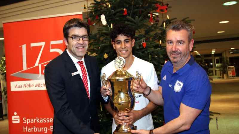 Sparkassen-Firmenkundenberater Stefan Behnke (von links), BSV- Talent Elias Saad und Turnier-Chef René Klawon mit dem Sieger-Pokal in der Filiale der Sparkasse Harburg-Buxtehude. | Foto: ein